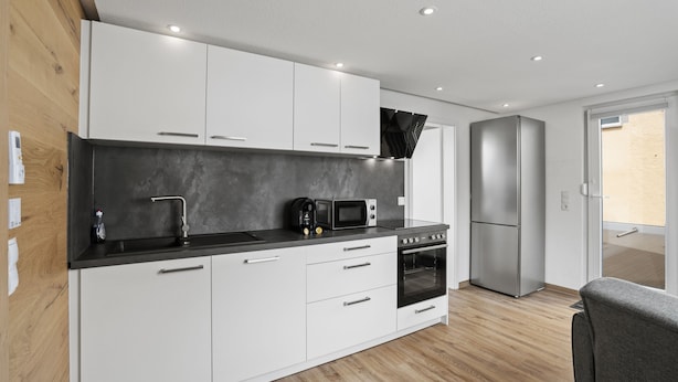 Una cocina moderna con armarios blancos, encimera negra y electrodomésticos de acero inoxidable.