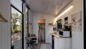 Une cuisine compacte équipée d’un four à micro-ondes, un petit coin repas avec une table et des chaises, et une vue sur l’extérieur grâce à une porte vitrée.