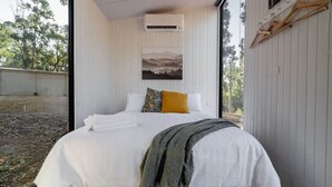 Une chambre à coucher avec un lit, du linge de lit blanc, un plaid gris et un tableau accroché au-dessus du lit.
