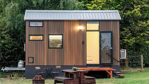 Una cabaña de madera compacta con puerta corredera, un pequeño porche y una mesa de picnic.