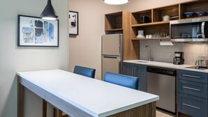 A modern kitchen with a white countertop, wooden cabinets, a stainless steel refrigerator, and a built-in dishwasher.