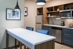 Una cocina moderna con encimera blanca, armarios de madera, un refrigerador de acero inoxidable y un lavavajillas integrado.