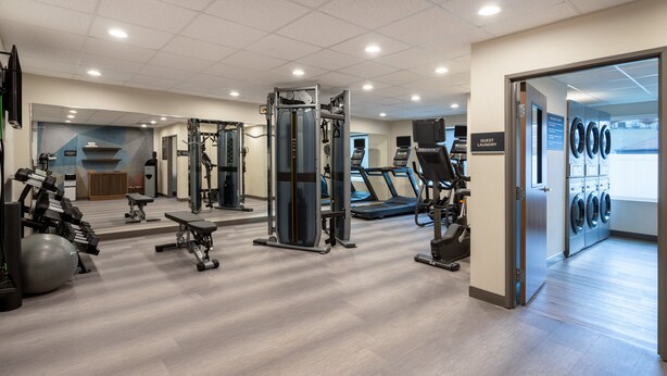 A gym with cardio machines, weightlifting equipment, and a wall-mounted TV.