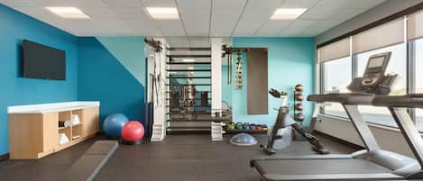 Un gimnasio con cintas de correr, pelotas de ejercicio y un televisor montado en la pared.
