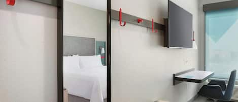 A hotel room with a bed, a desk, a chair, a TV, and a mirror.