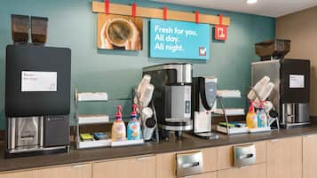 A coffee station with multiple coffee machines, a sign indicating fresh coffee availability, and dispensers for coffee creamer and milk.
