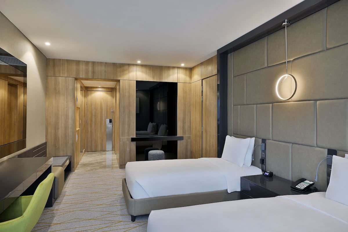 Ein modernes Hotelzimmer mit zwei Betten, einem Schreibtisch und einer Sitzecke.