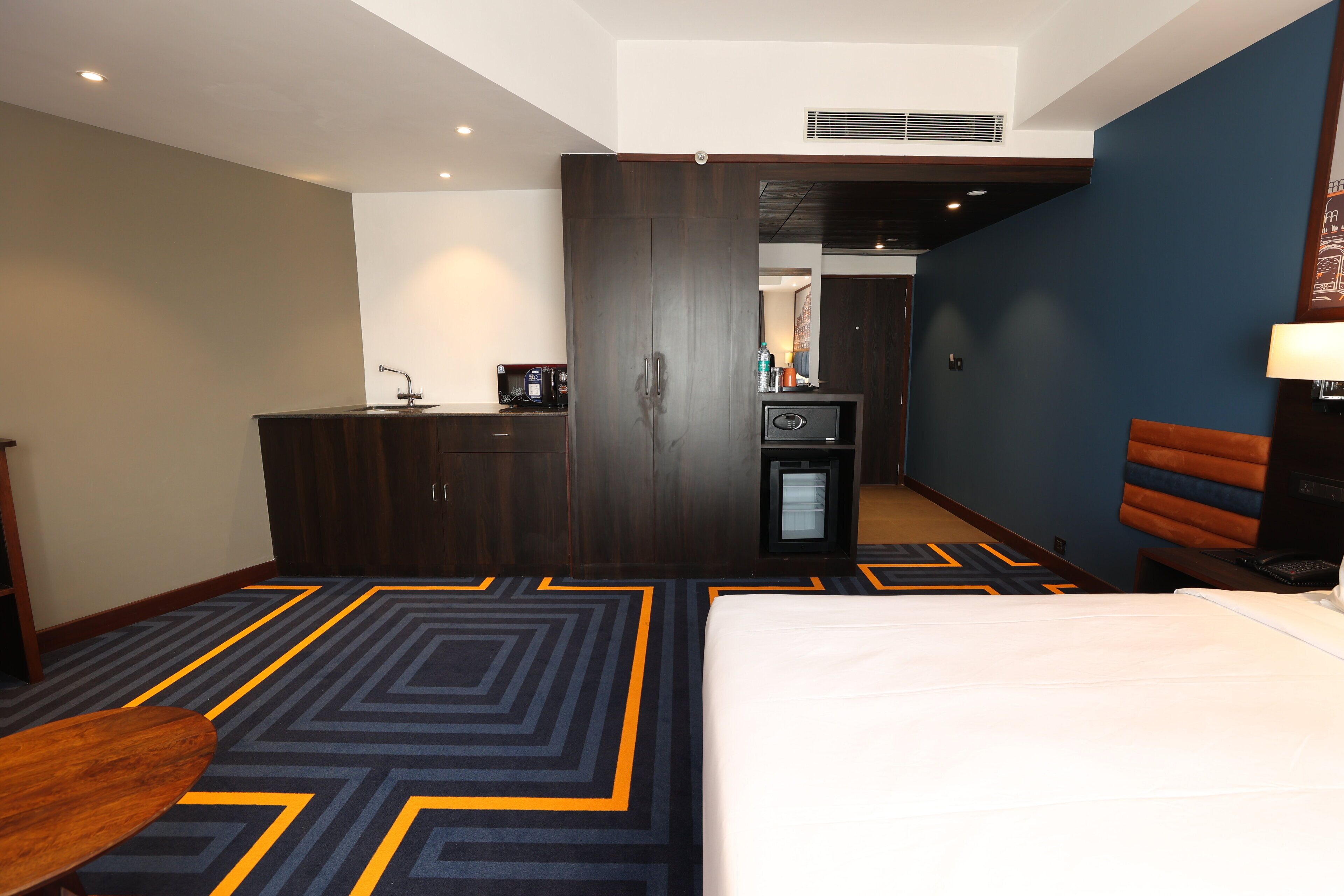 A hotel room with a bed, a desk, a minibar, and a wardrobe.