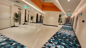 A hotel corridor with a geometric patterned floor, white walls, and a ceiling with recessed lighting and an orange accent. - Holiday Inn Express & Suites Jaipur Gopalpura by IHG (Jaipur)
