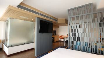 Una habitación de hotel moderna con un separador de vidrio, un televisor de pantalla plana, techo de madera y una zona de comedor con mesa y sillas.