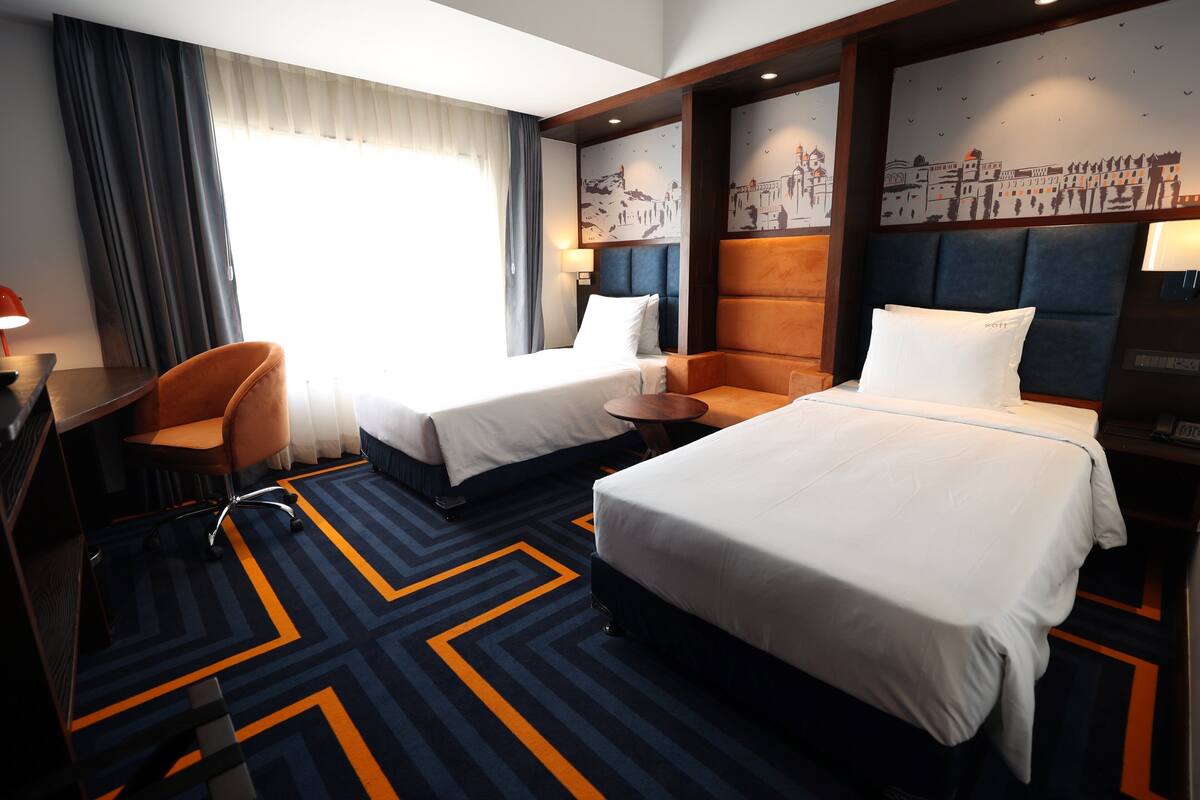 Une chambre d’hôtel avec deux lits, un bureau, une chaise et une petite table.