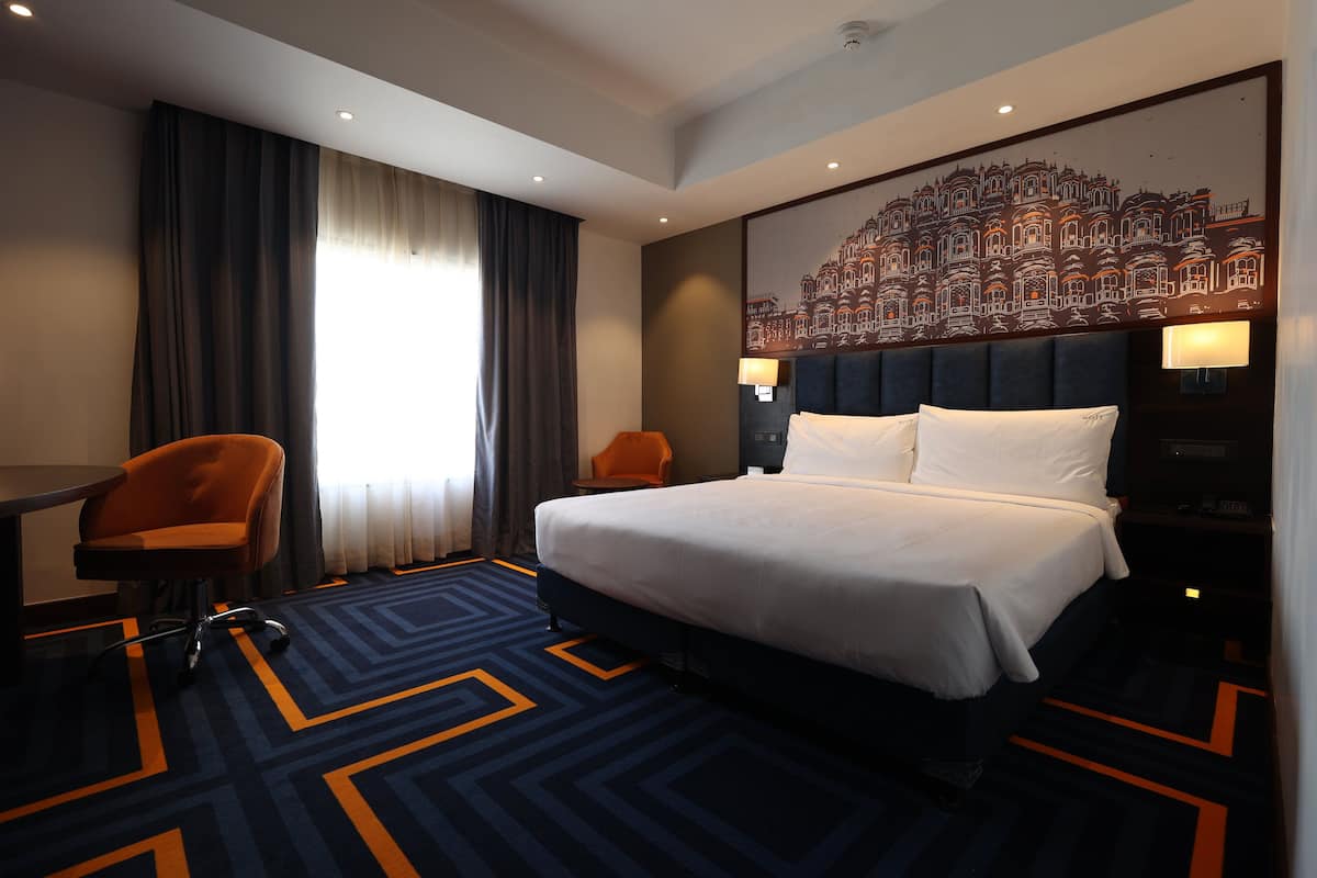 Une chambre d’hôtel avec un grand lit, un bureau, une chaise orange et un téléviseur fixé au mur.