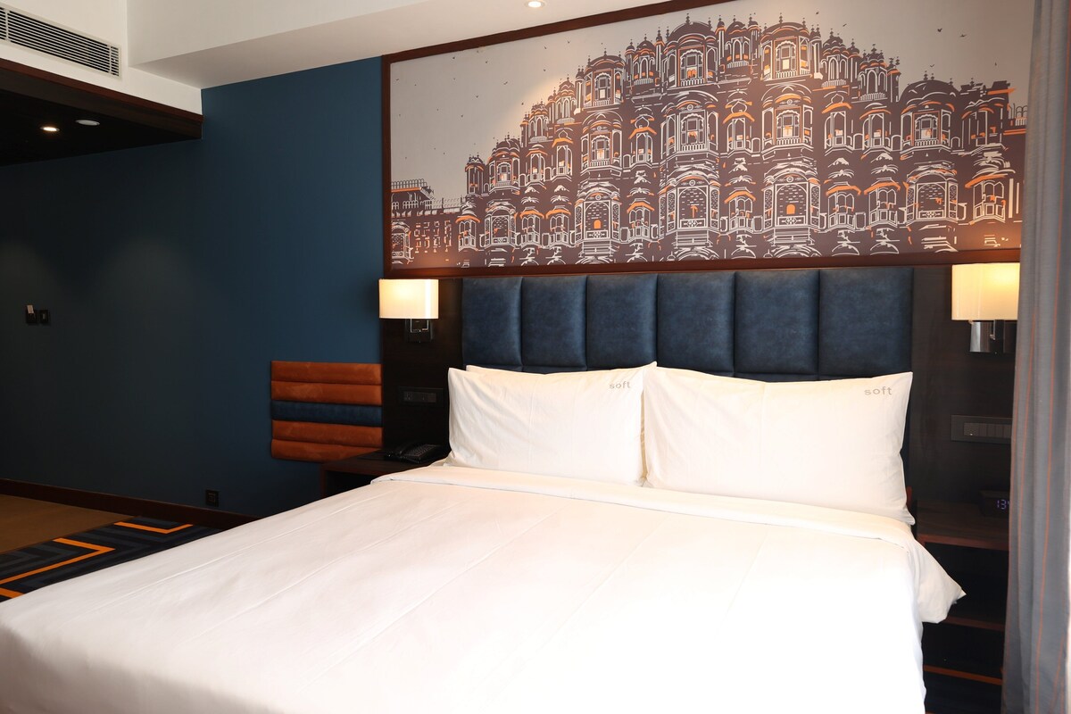 A hotel room with a large bed, a headboard, two bedside lamps, a wall-mounted artwork, and a nightstand with a phone.
