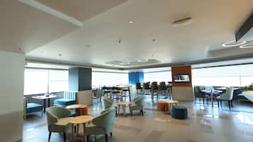 A spacious indoor area with multiple seating arrangements, including tables and chairs, and a large window providing natural light.