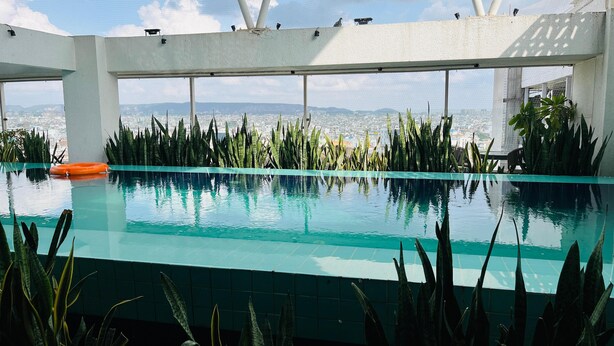 A rooftop infinity pool with a city view, surrounded by tall plants and a white structure. - Holiday Inn Express & Suites Jaipur Gopalpura by IHG (Jaipur)