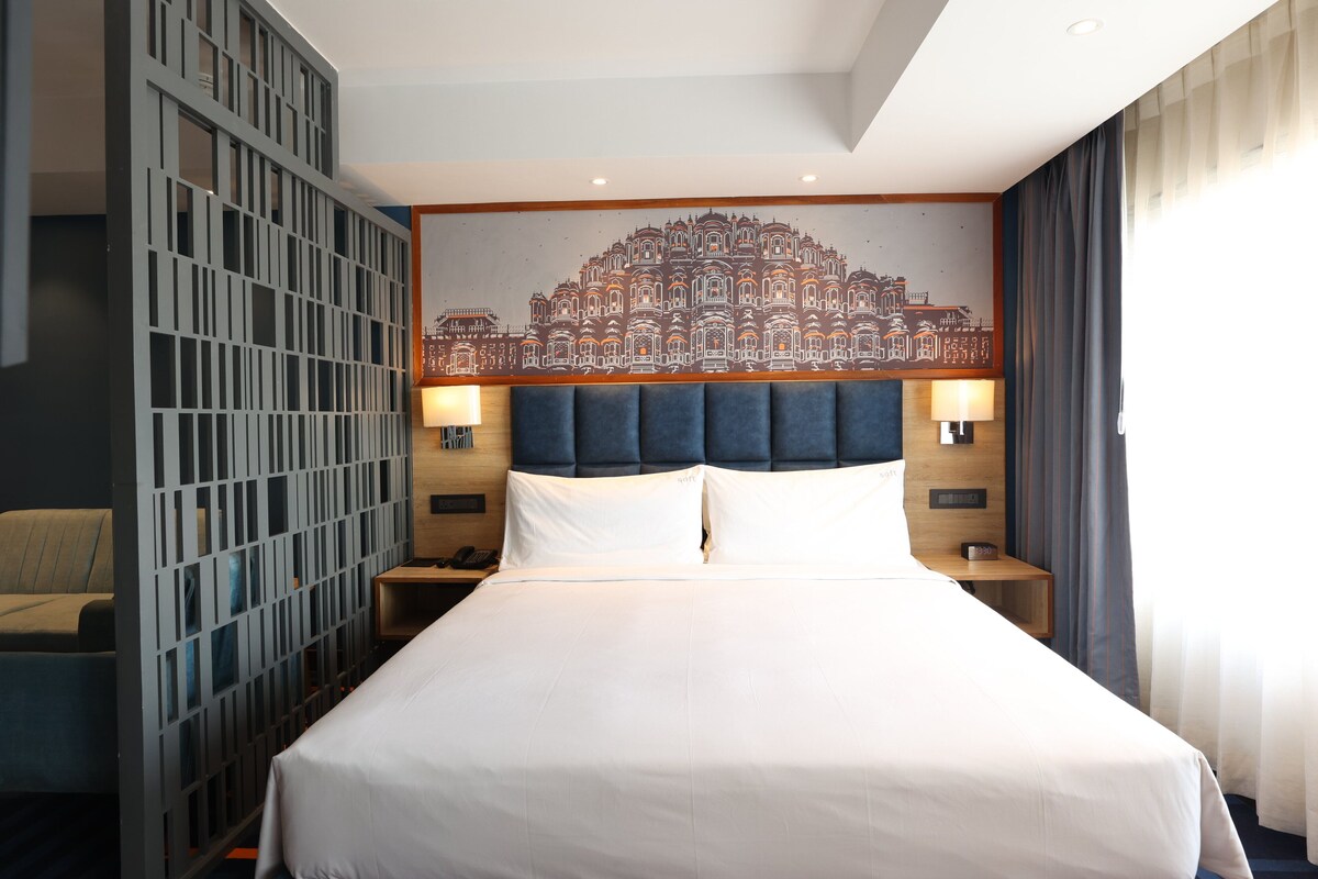 A hotel room with a large bed, a headboard with a cityscape mural, two bedside lamps, and a wooden nightstand with a phone.