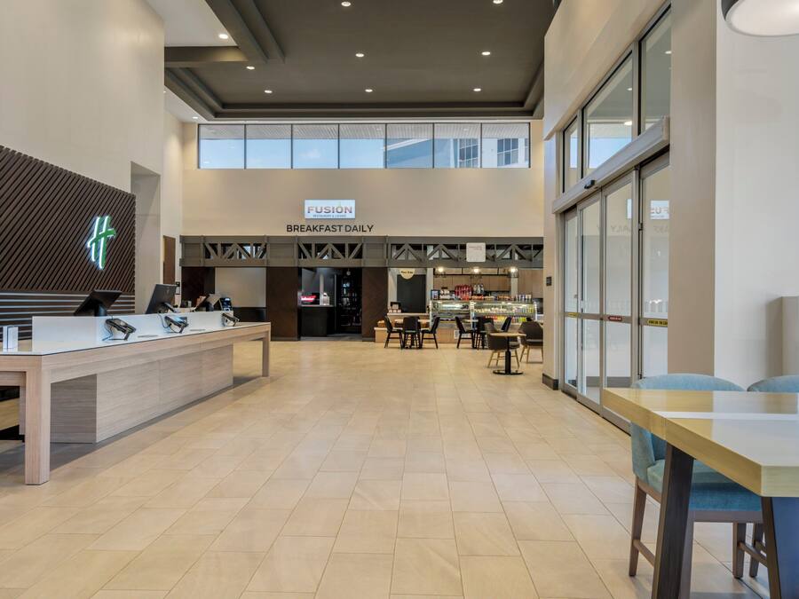 Un vestíbulo de hotel moderno con mostrador de recepción, zona de desayuno y un área de estar con mesas y sillas.