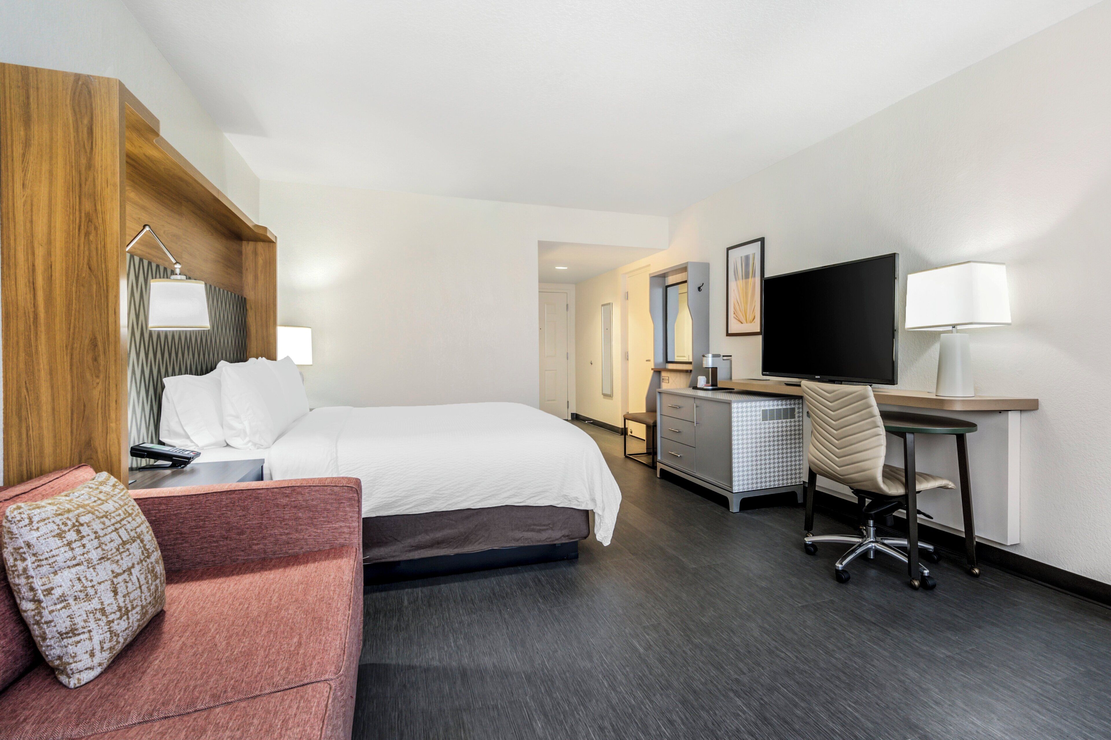 A hotel room with a bed, a desk, a chair, a television, and a sofa.