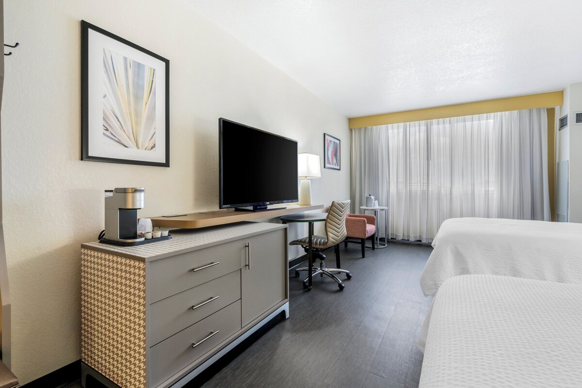A hotel room with a bed, a desk with a computer, a chair, a television, and a coffee maker.