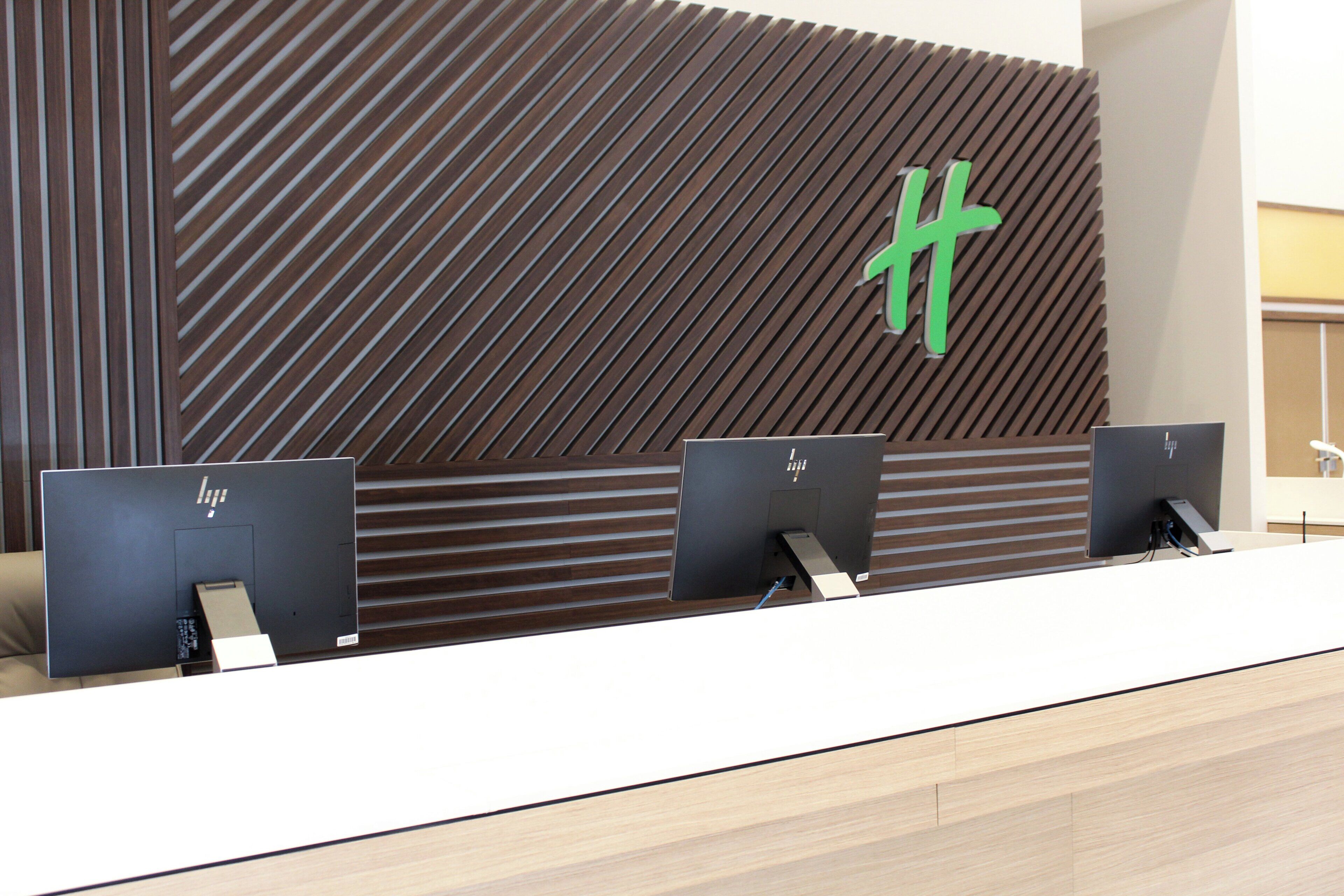 Un mostrador de recepción de diseño moderno, con un panel de madera en la pared que presenta un patrón geométrico y un logotipo verde destacado.