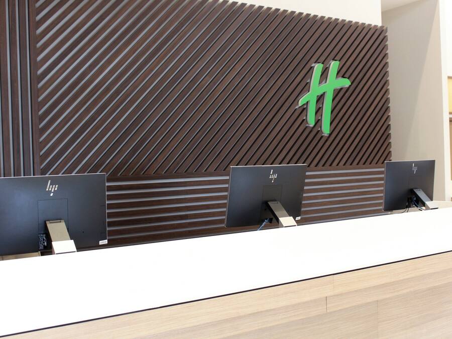 Un mostrador de recepción de diseño moderno, con un panel de madera en la pared que presenta un patrón geométrico y un logotipo verde destacado.
