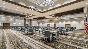 A conference room with multiple tables and chairs, a patterned carpet, and modern lighting fixtures. - Holiday Inn Orlando International Dr-ICON by IHG (Orlando)