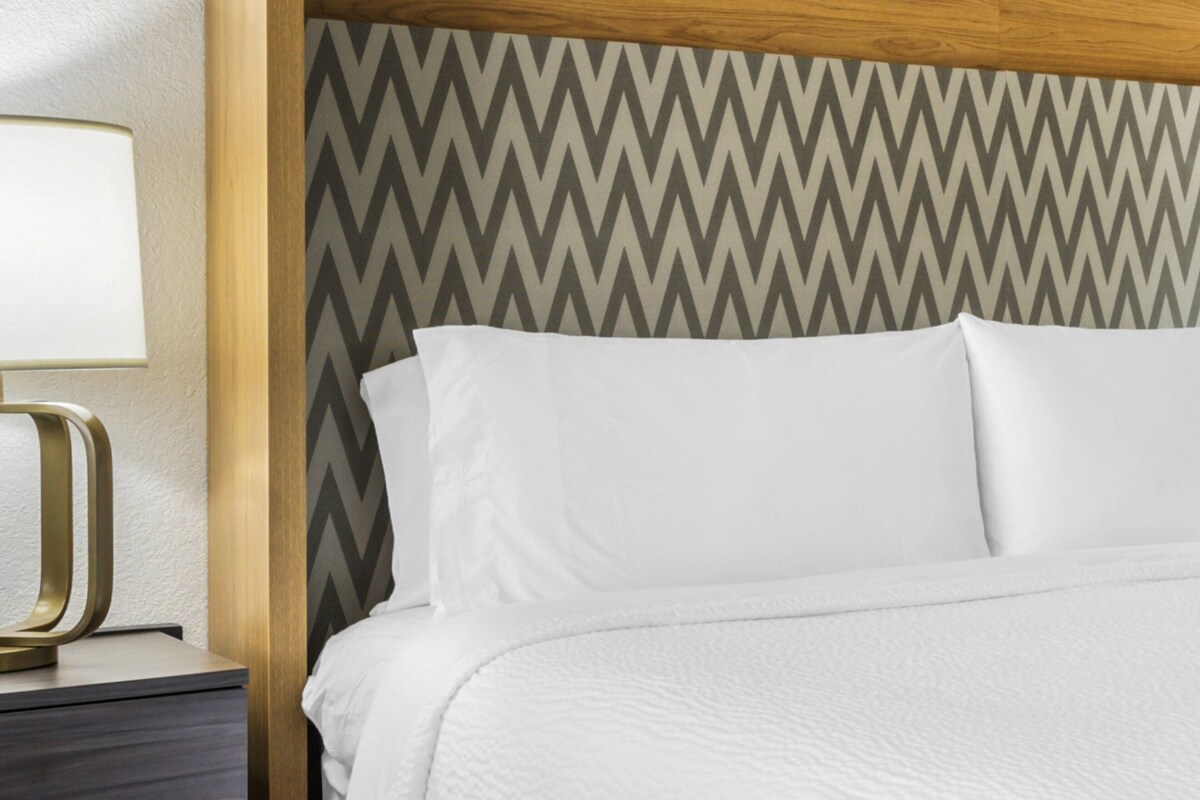 A neatly made bed with white linens, a wooden headboard with a chevron pattern, and a bedside table with a lamp.