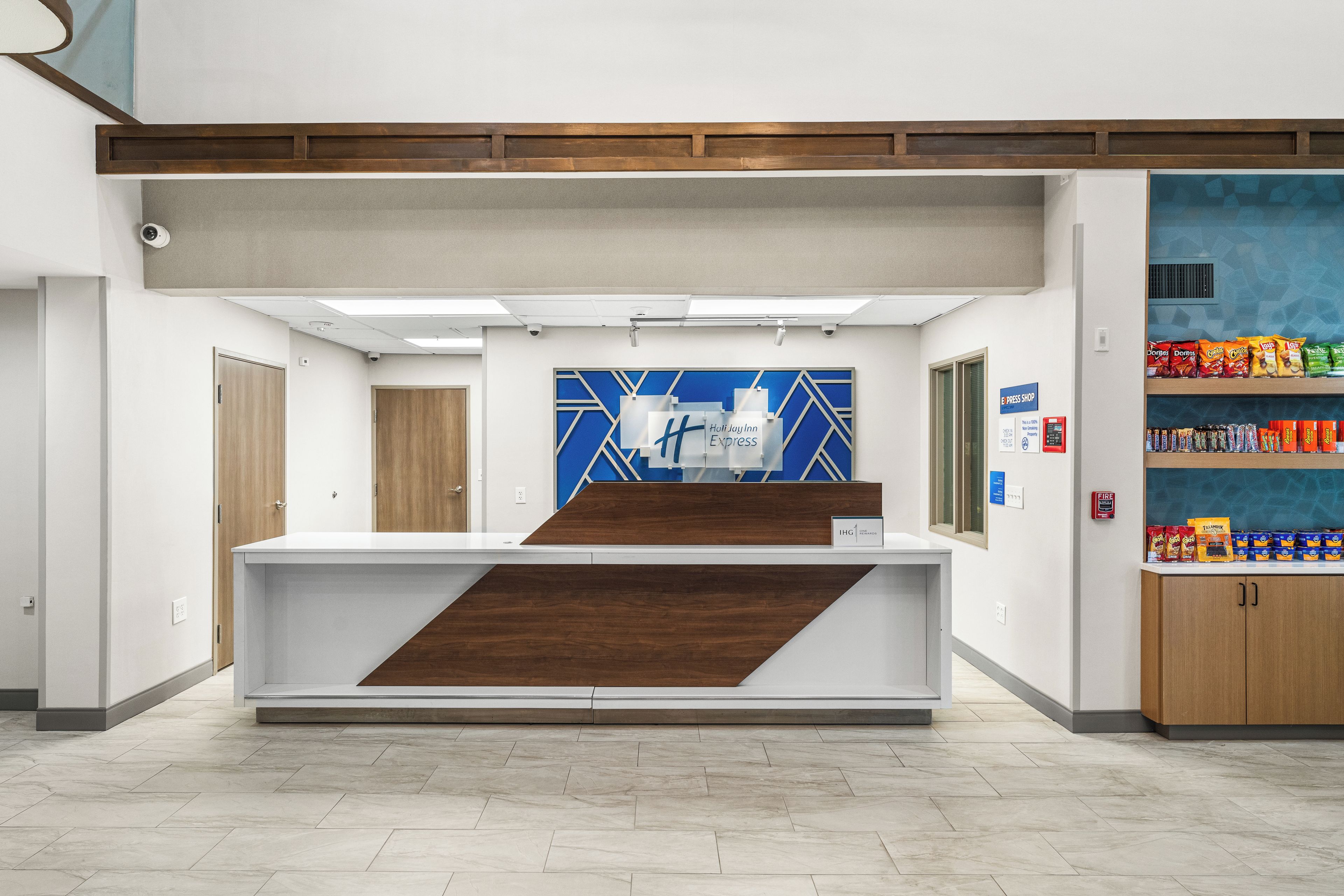 A reception desk with a blue and white geometric wall design, a fire extinguisher, and a snack shelf.