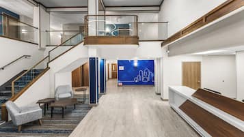 Un hall espacioso con techo alto, una escalera, una zona de estar y una recepción.