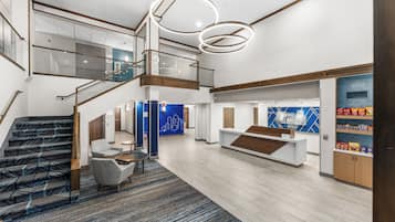 Un amplio vestíbulo de hotel con escalera, zona de estar y mostrador de recepción.