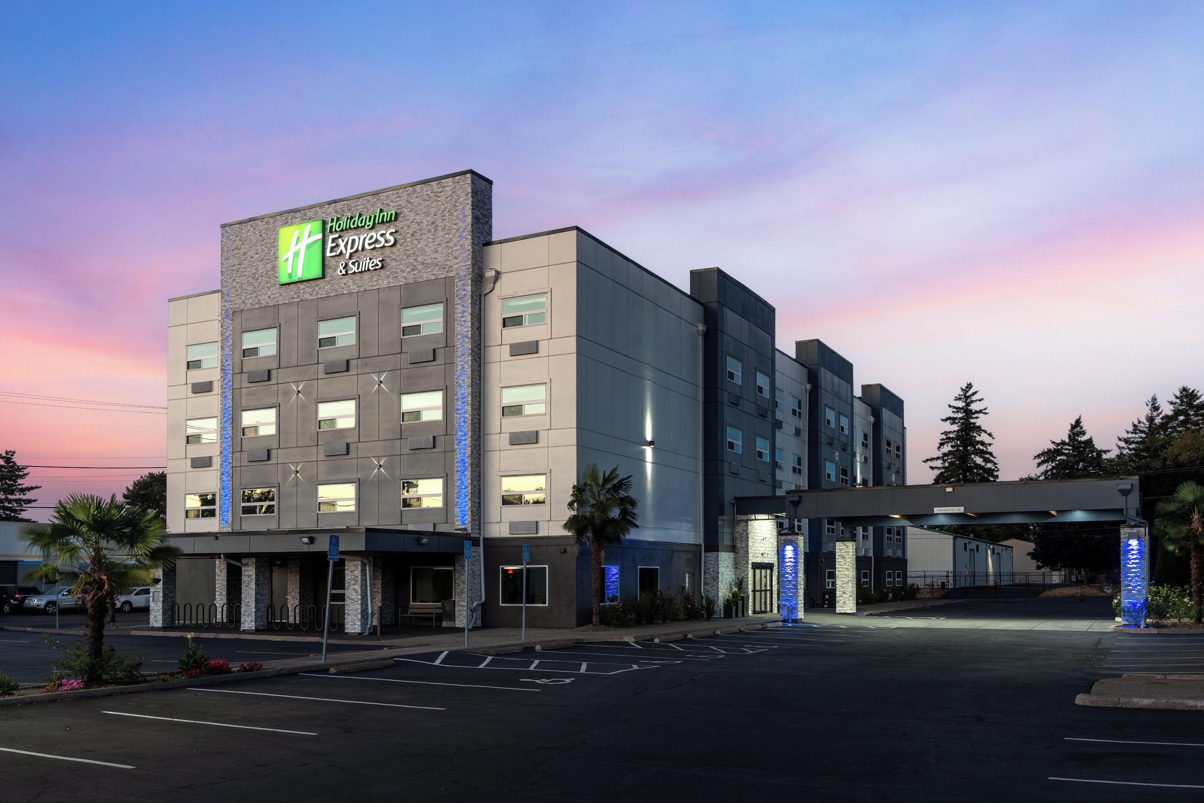 Un hotel Holiday Inn Express & Suites con un diseño moderno, que cuenta con un letrero llamativo y un estacionamiento.