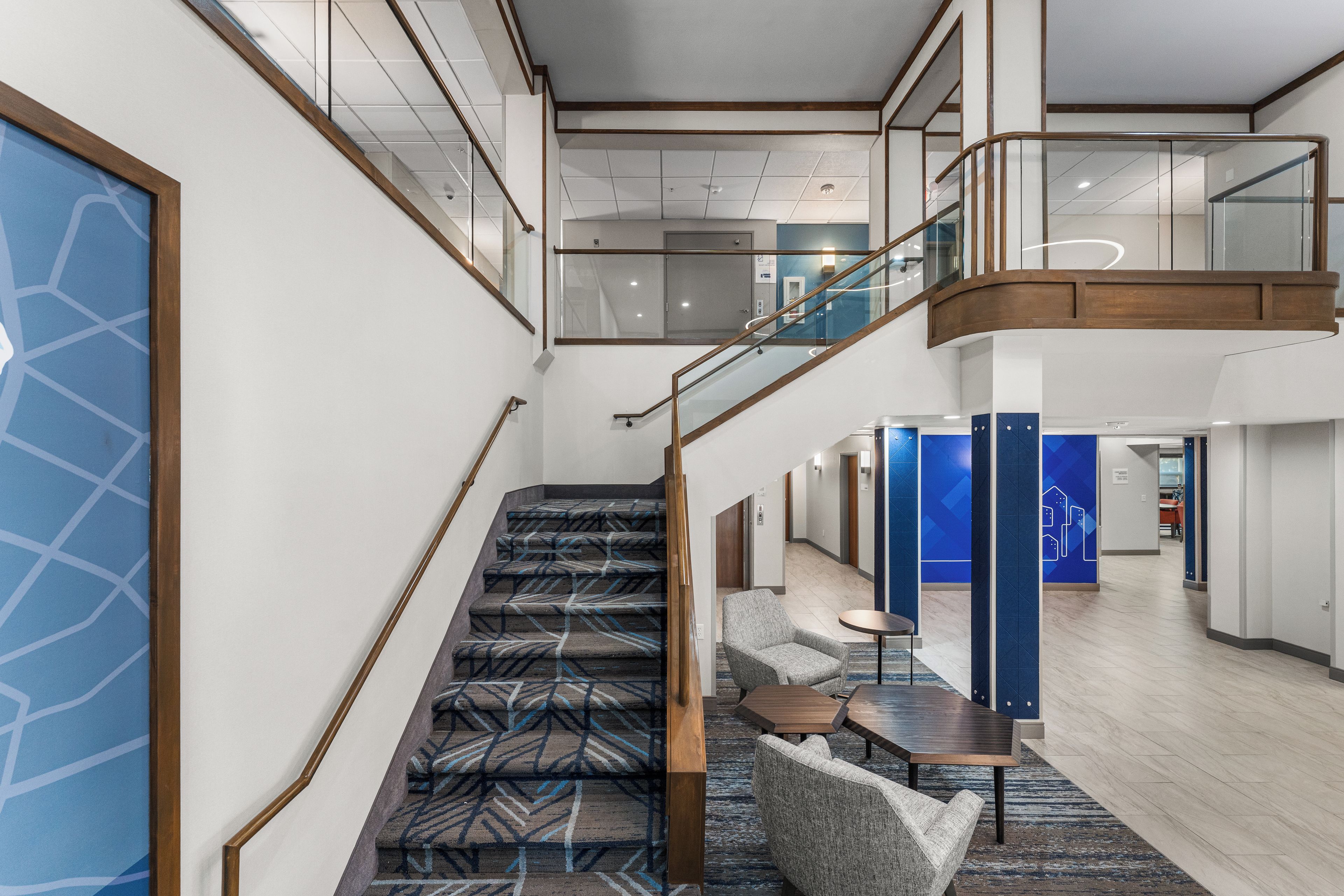 A modern hotel lobby with a staircase, seating area, and a view of the upper floor.