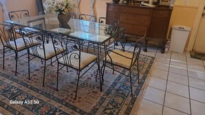 Un coin repas comprenant une table à plateau en verre, des chaises en métal, un tapis à motifs, une horloge, une plante en pot et un meuble.