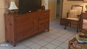 Un salon avec un meuble en bois, un téléviseur, un fauteuil et une table basse en verre.