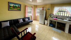 A living room with a sofa, a dining table, and a kitchen area with a refrigerator and sink. - Miravalles Volcano House (Mogote de Bagaces)