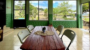 A dining area with a wooden table, chairs, and large windows offering a view of greenery and trees. - Miravalles Volcano House (Mogote de Bagaces)