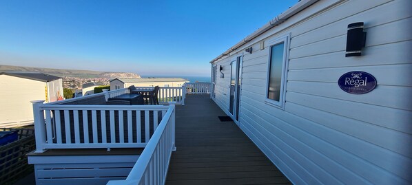 Een overdekt terras met uitzicht op zee, een wit gebouw met een 'Regal Holiday Homes' bord en een witte balustrade.