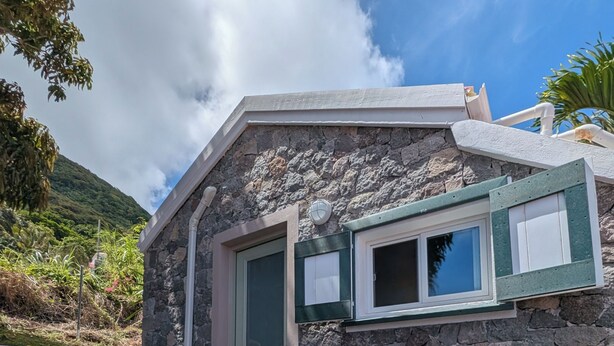 A stone building with a stone staircase, a Samsung air conditioner, and two black metal chairs on a tiled patio. - Peter Hytte is close to everything at great price! (Windward Side)