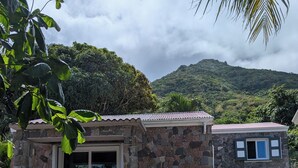 A stone building with a balcony, surrounded by greenery and a mountainous backdrop. - Peter Hytte is close to everything at great price! (Windward Side)