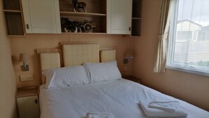 Una cama bien tendida con sábanas y toallas blancas, cabecera de madera y una ventana con cortinas.