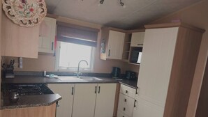Cocina compacta con estufa a gas, pileta y muebles blancos.
