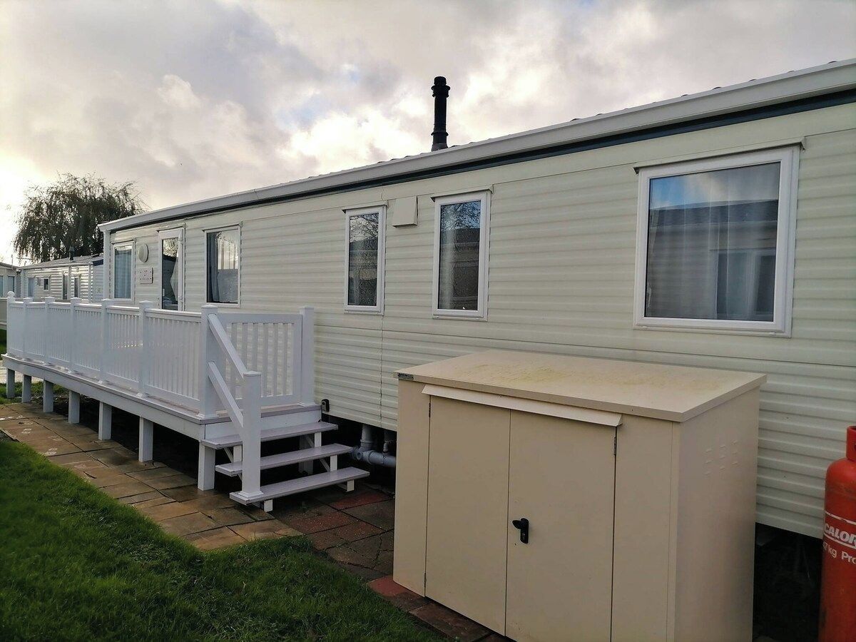 A mobile home with a white exterior, a small porch with a white railing, and a beige utility cabinet.