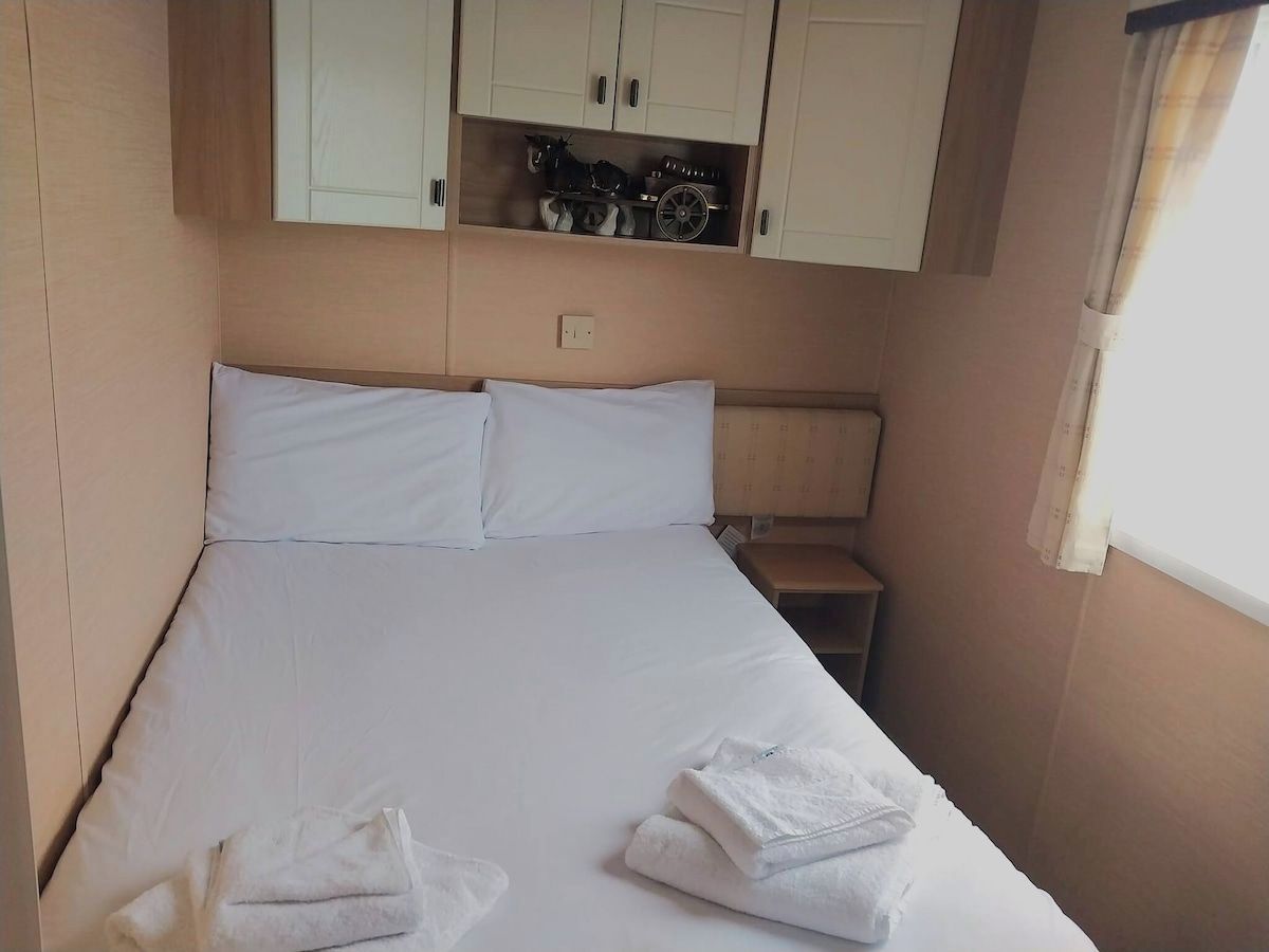 A single bed with white linens, a nightstand, and a shelf above the bed with various items.