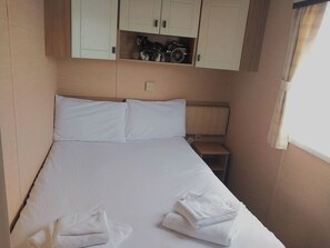 Un lit simple avec du linge de lit blanc, une table de chevet et une étagère au-dessus du lit, sur laquelle sont disposés divers objets.