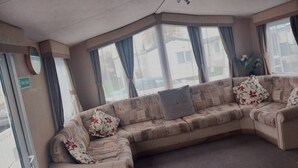 Un salón en esquina con un sofá seccional color beige, una mesita y un ventanal con cortinas.
