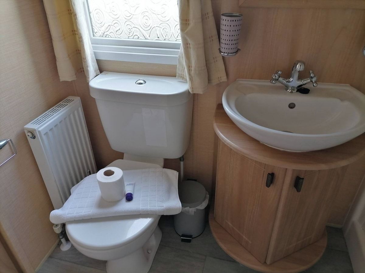 Une petite salle de bain comprenant des toilettes, un lavabo et une fenêtre avec des rideaux.