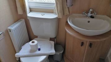 Une petite salle de bain comprenant des toilettes, un lavabo et une fenêtre avec des rideaux.