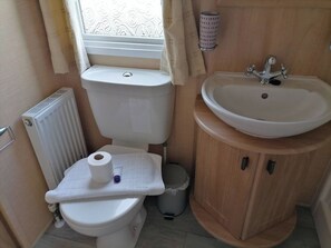 Une petite salle de bain comprenant des toilettes, un lavabo et une fenêtre avec des rideaux.