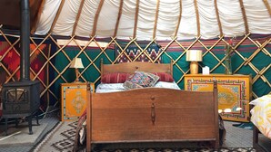 A traditional yurt interior with a wooden bed, a small stove, and patterned textiles. - Eco Glamping immersed in nature, ideal for family holidays andromantic getaways! (Whitegate)