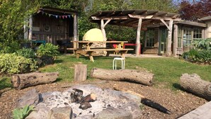 A rustic outdoor setting with a wooden structure, a fire pit, and a covered picnic table. - Eco Glamping immersed in nature, ideal for family holidays andromantic getaways! (Whitegate)